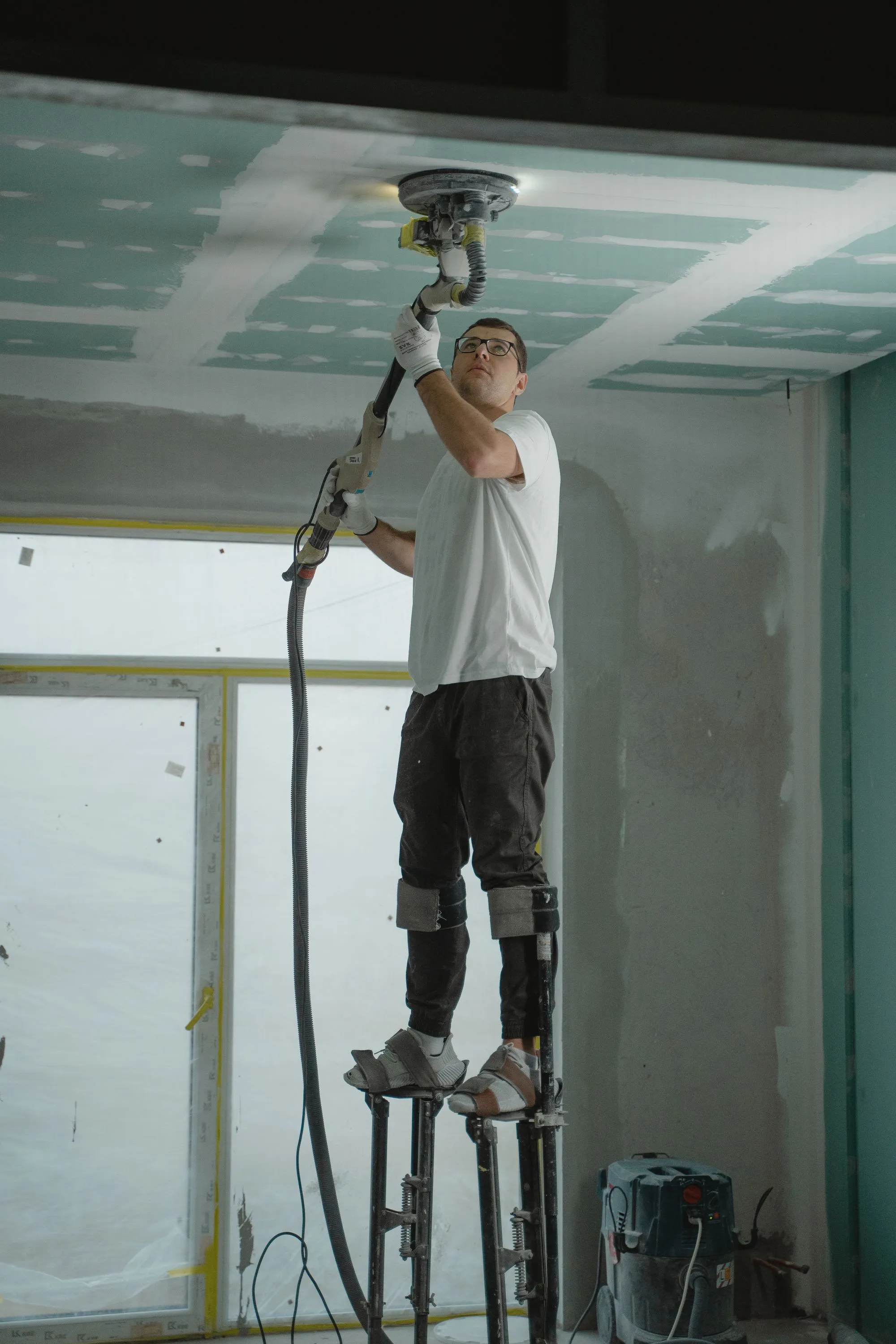 Drywall finisher on stilts sanding a commercial ceiling